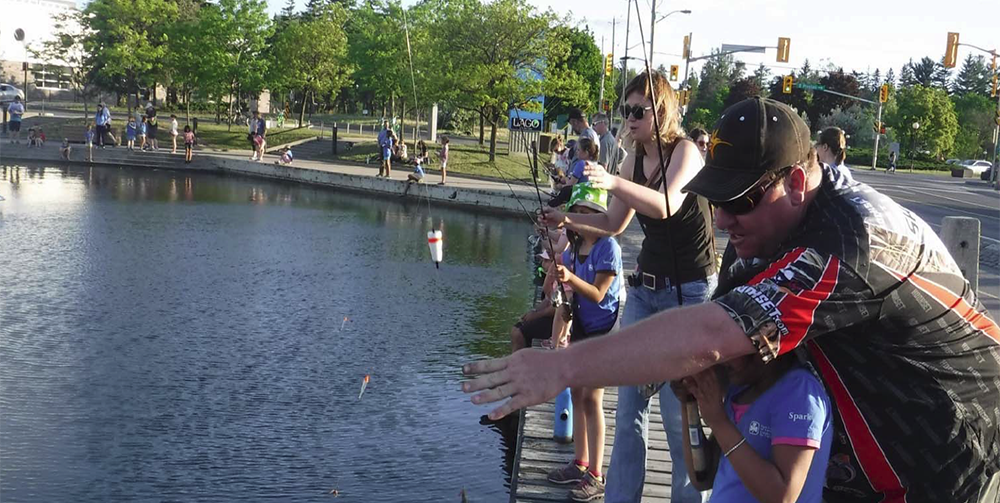 People fishing along park pond walkway